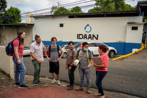 People speaking on a street sidewalk, smiling.