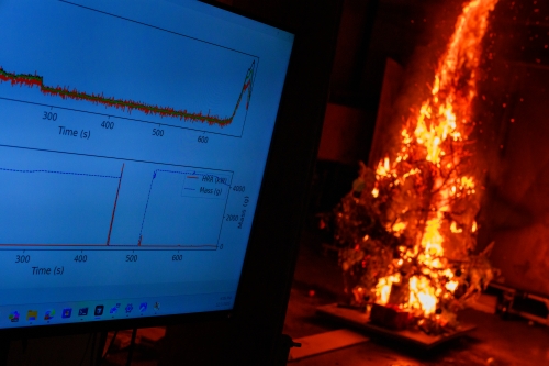 Christmas tree engulfed in flames inside a laboratory. In the foreground, a computer screen displays a line graph with measurements of the intensity of the fire over time