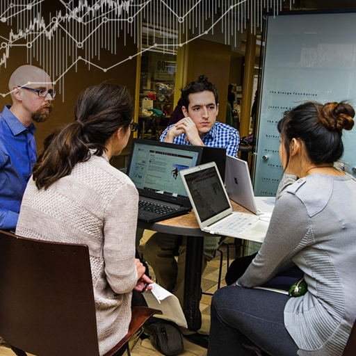 WPI Business School professors work together around a desk with laptops in front of them.