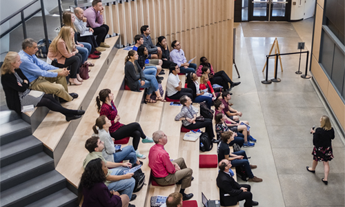 WPI professor gives a talk in front of a large, wall-sized screen in front of people in amphitheater-style seating.