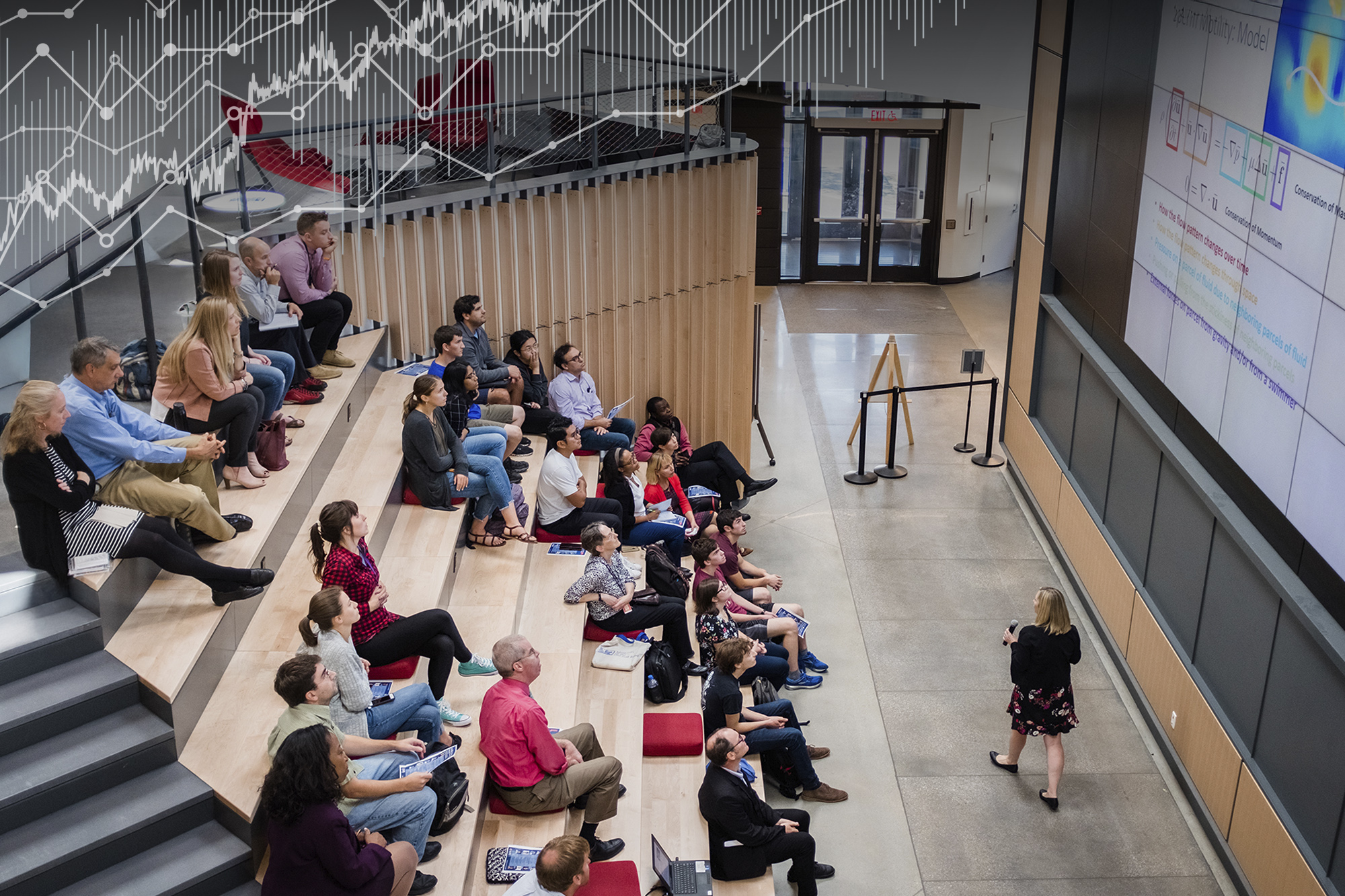 WPI professor gives a talk in front of a large, wall-sized screen in front of people in amphitheater-style seating.