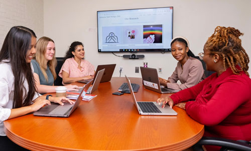 WPI Business Analytics students sitting around a table in front of a projected screen showing various data.