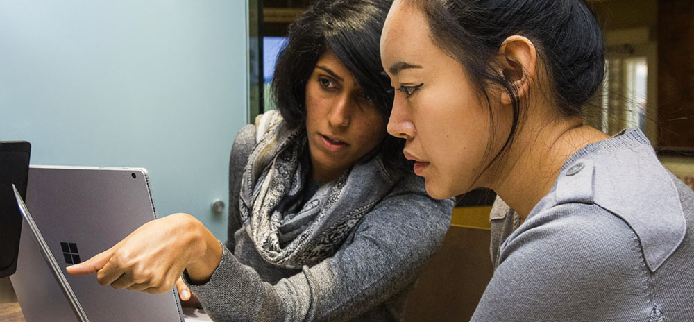 Two female WPI Business School students looking at course work on laptops.