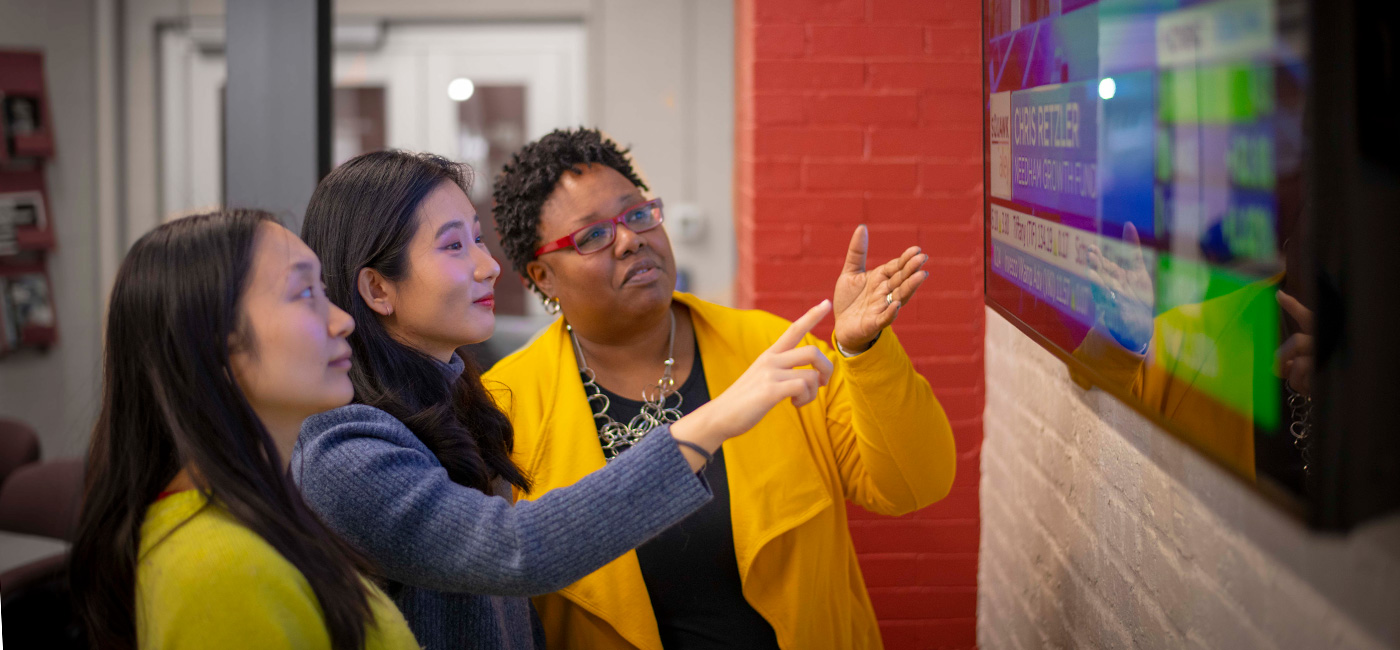 Professor and students looking at stock market news on a television.