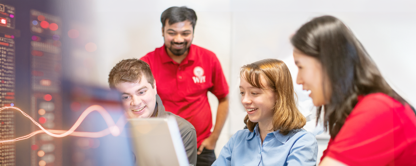 A few students with their professor gathered together looking at a screen and working on a problem together.