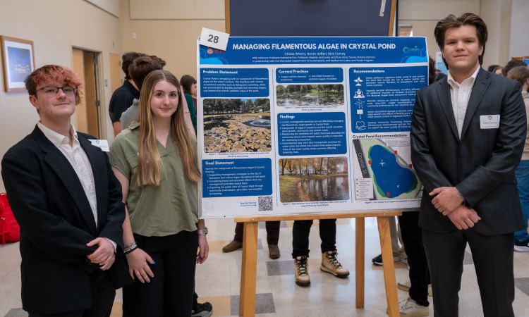 three students stand beside their poster showing undergraduate research