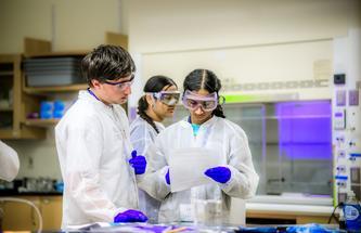 three students in white lab coats in a lab