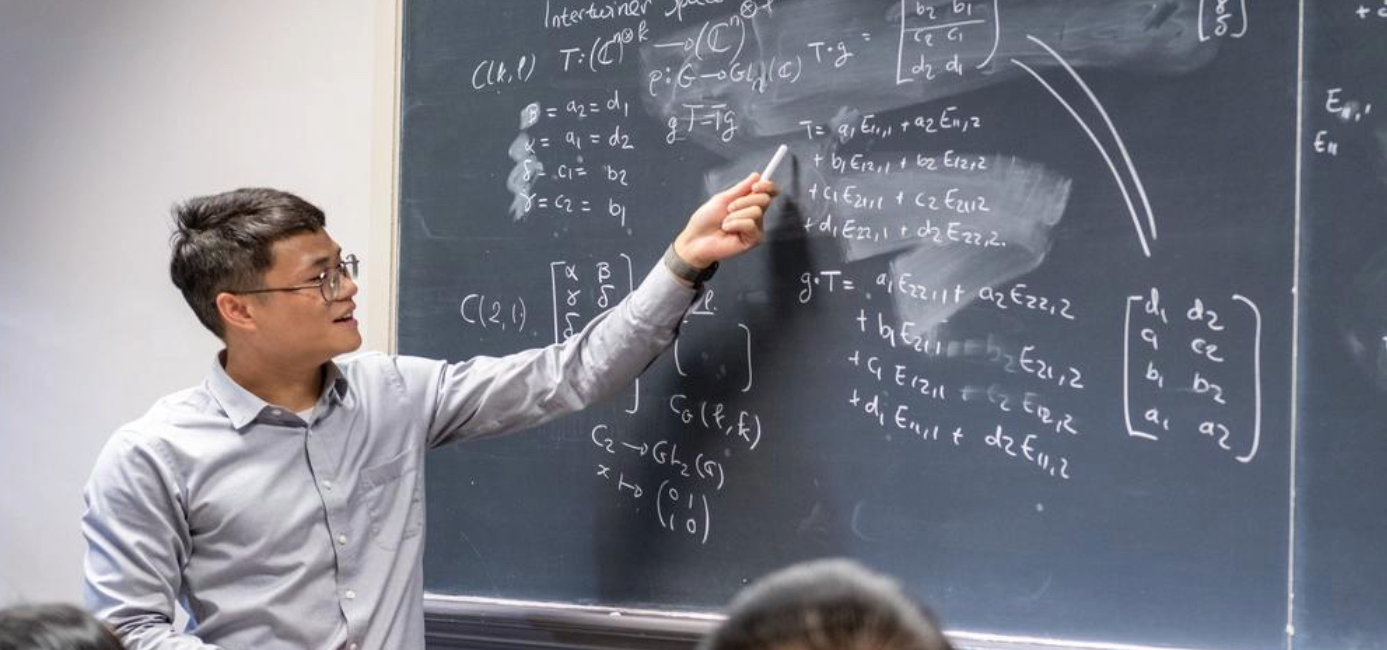 Man holding chalk pointing to chalkboard with math equations