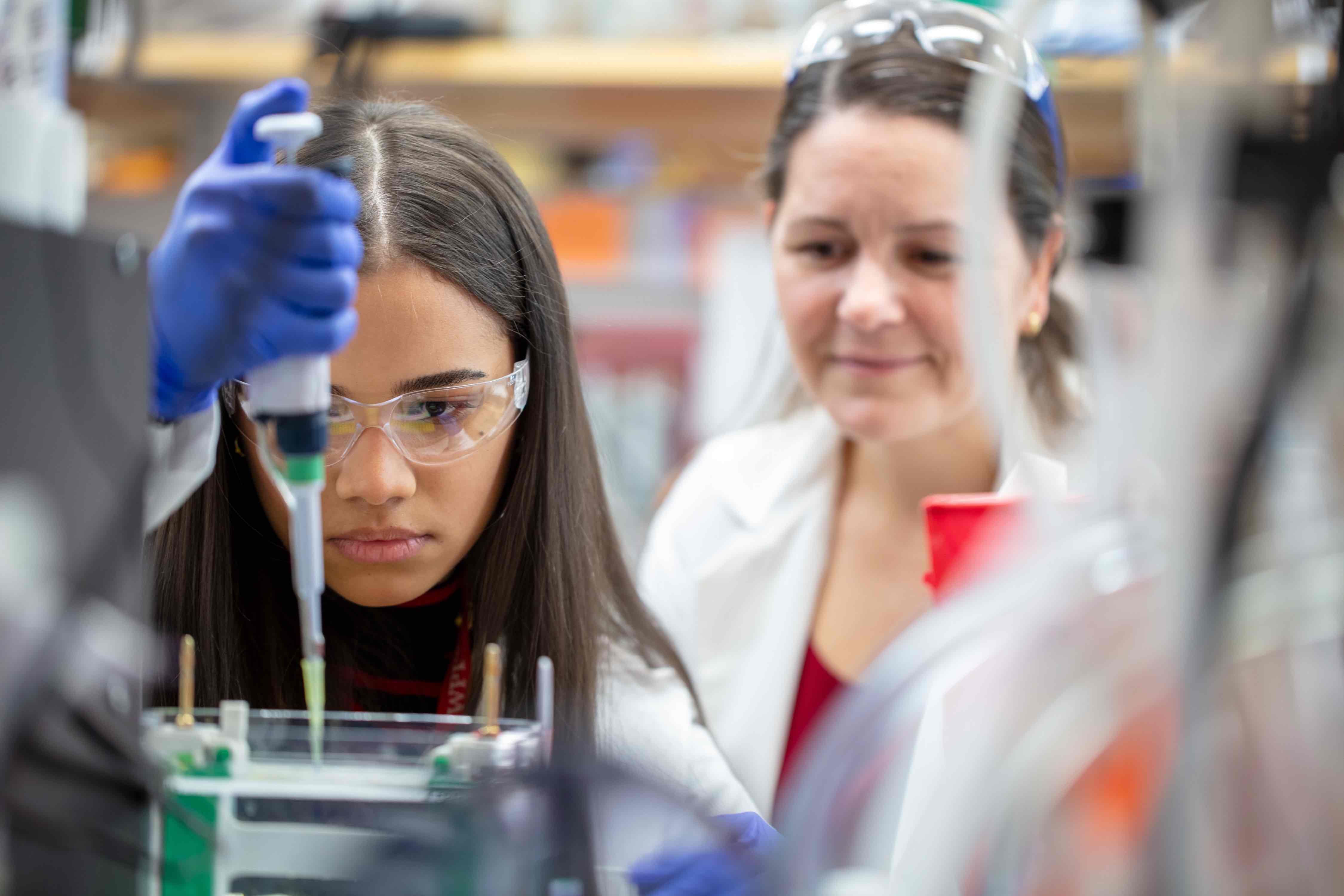 2 people doing chemistry and dropping liquid into a beaker