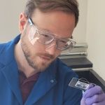 Man in lab coat holds a lab slide.