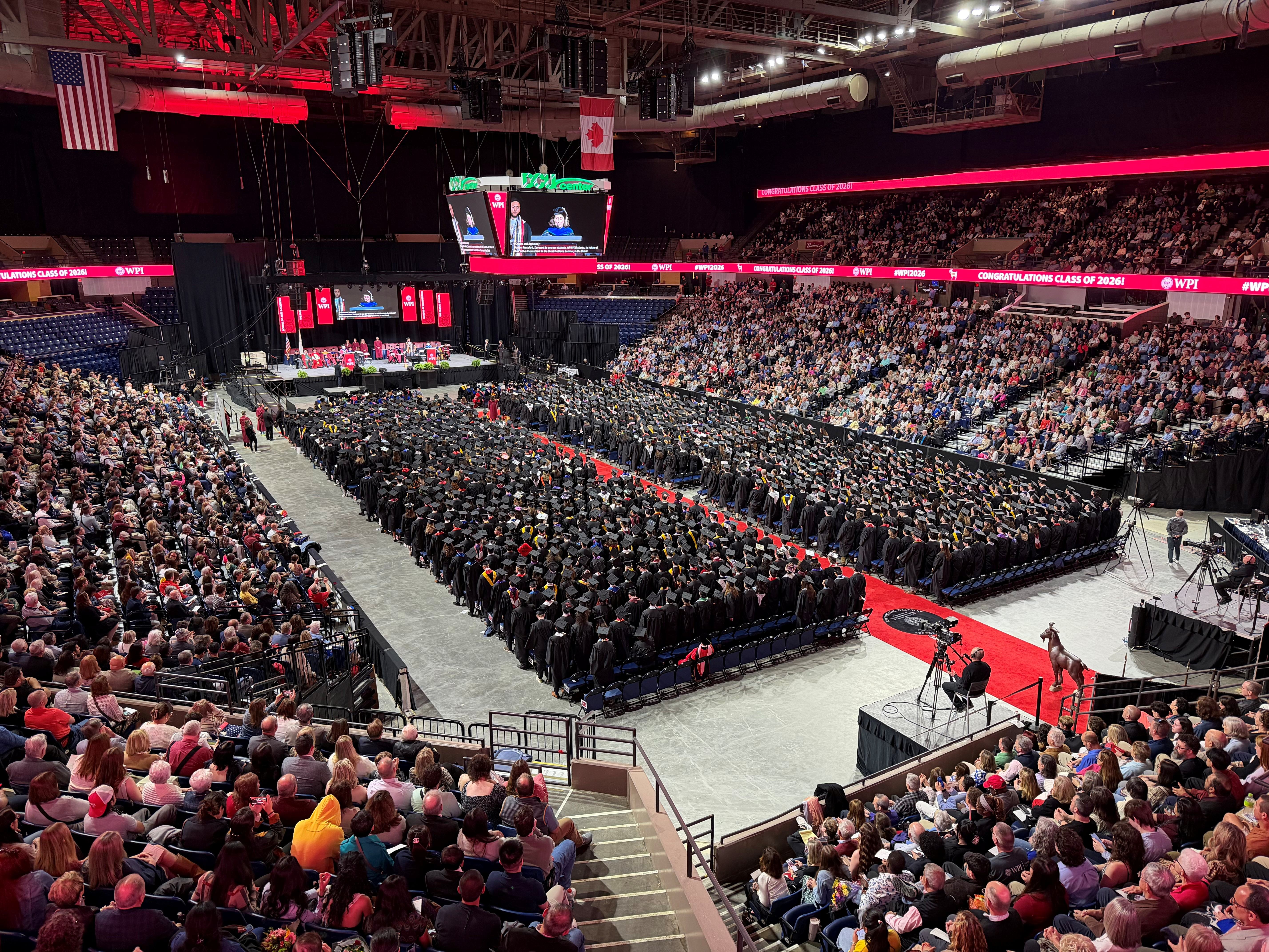 students wearing caps and gowns sitting on arena floor at commencement