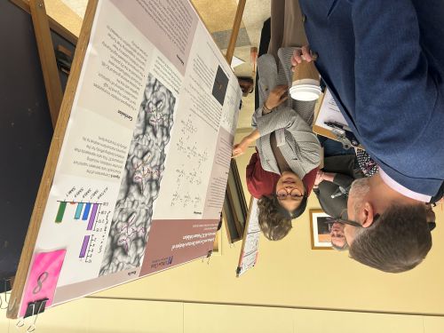 student pointing to her poster with faculty watching