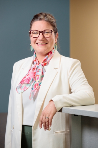 Woman smiling in an office building with one arm resting on a tall table