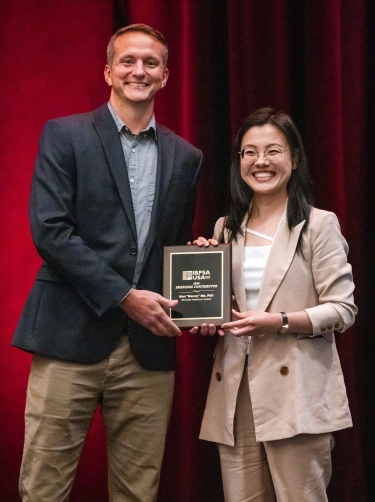 Professor receiving an award, holding a plaque, standing next to the award presenter