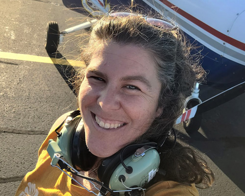 Amanda Gallerani wearing an aviation headset in front of a small aircraft, reflecting her hands-on STEM and science education work.