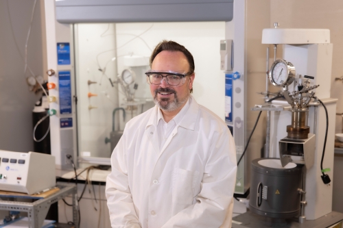 Professor in lab coat smiling in a laboratory in front of equipment
