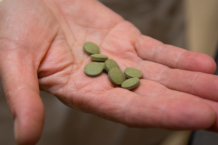 a hand holding a group of green tablets alt
