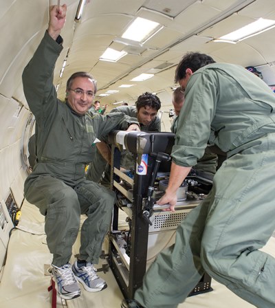 Jamal Yagoobi, left, floats beside a prototype of the cooling pump developed in his lab during a test flight on a NASA zero-gravity aircraft