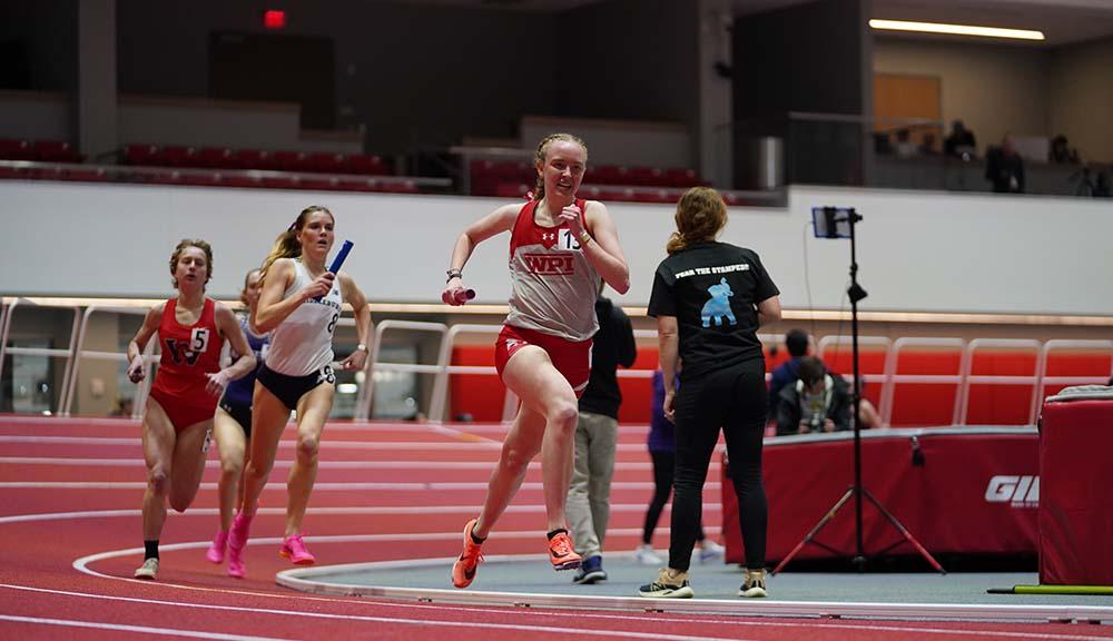 A member of WPI's track and field team runs past members of opposing teams.