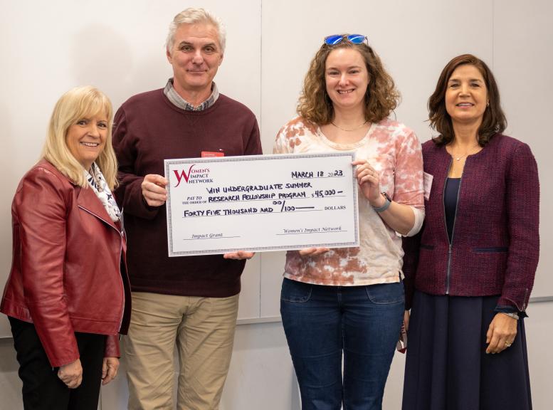 three women and a man pose with large check