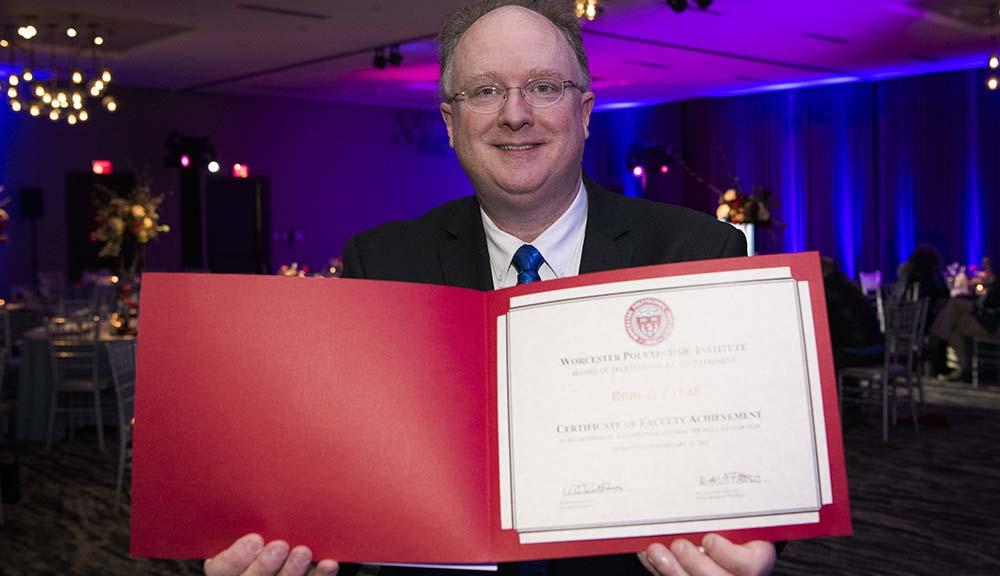 A WPI faculty member holds up a certificate.