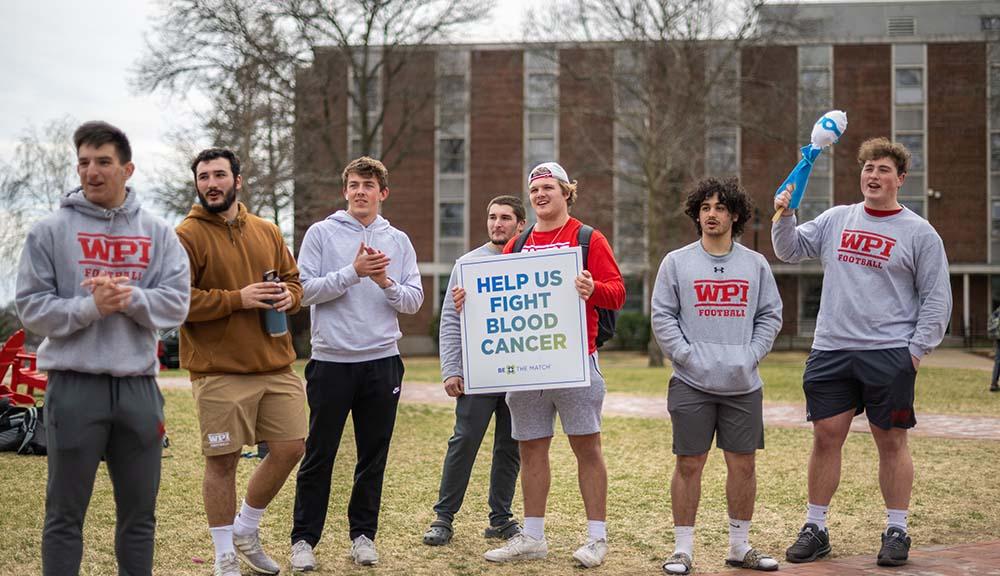 Members of the football team stand on the Quad holding a sign that says "Help us fight blood cancer."