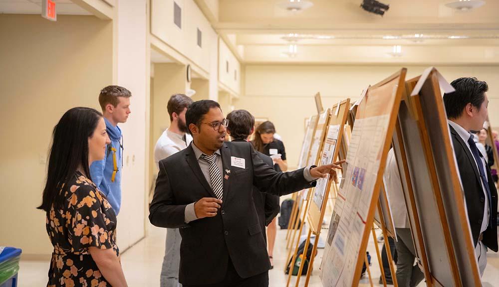 A student presents their work on a poster board in the Odeum.