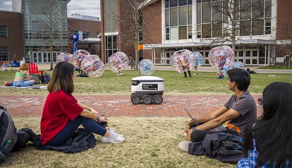 Students watch the food robots travel along the Quad.