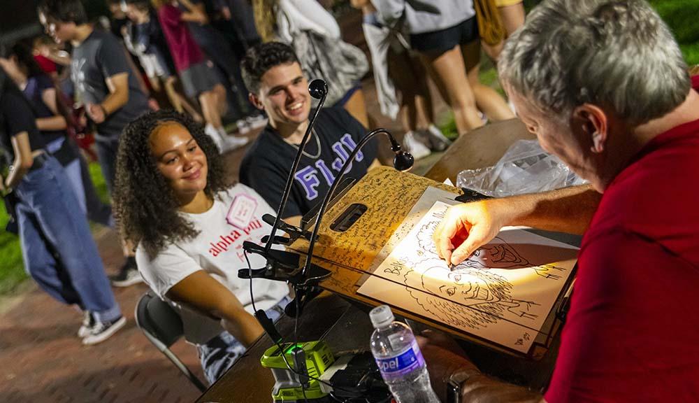 Students get a caricature of themselves done during Greek Carnival on the Quad.