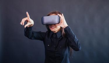 A woman uses a virtual reality headset against a dark background.