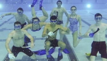 Seven students are underwater with snorkels, goggles, and their underwater hockey equipment, smiling at the camera.