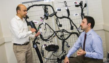 Alex Wyglinski and Raghvendra Cowlagi discuss the technology involved in autonomous vehicles, with a wiring harness for a 2014 Chevy Impala in the background. 