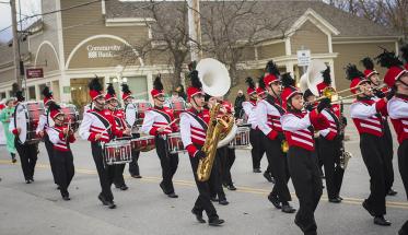 The WPI Pep Band marches down Main Street in Manchester, Vermont, wearing their black, red, and white uniforms and playing a variety of instruments.