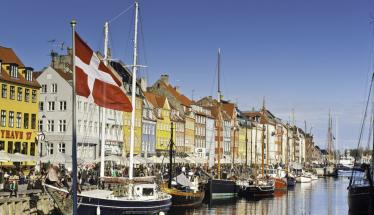 A photo of a river in Copenhagen lined with boats. Colorful homes also line the river behind the boats.