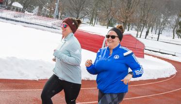 Meredith Merchant and Jessica Karner run along the WPI track together. They're both smiling, dressed in workout clothes, and are wearing sunglasses.