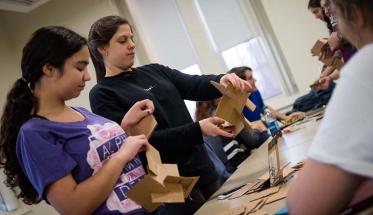 Two students hold pieces of cardboard and work to connect them together as part of an engineering project.