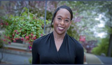 Margot Lee Shetterly smiles in front of a background of greenery and flowers. She's wearing a black shirt, and has her hair pulled back.