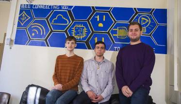 Three members of We Art Good stand in front of a mural their club created for IEEE.