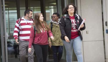 Four students exit a building on WPI's campus. Most are wearing WPI gear, and they're conversing with each other.