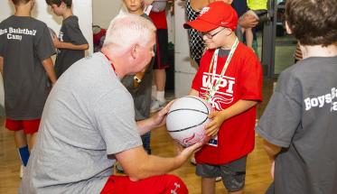 "Fist Bump Kid" Liam Fitzgerald accepts a basketball from a member of the WPI basketball coaching staff.