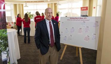 Greg Snoddy stands in the Rubin Campus Center next to a poster board that says "Giving Day is Nov. 27! What does 'giving back' mean to you?"