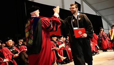 A graduate in cap and gown receives a high five from Arthur Heinricher, also in cap and gown
