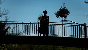 A silhouette of a graduate standing on top of Earle Bridge.