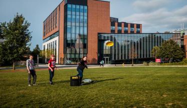 Students play frisbee on the Quad with the Foisie Innovation Studio in the background.