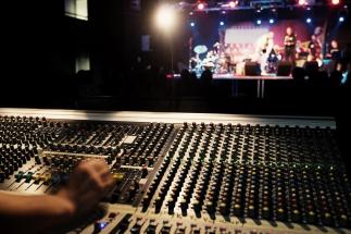 A person works a soundboard while musicians play.