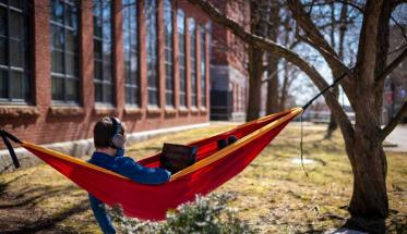 A student lounges in a hammock while working on a laptop.