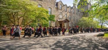 graduates in caps and gowns crossing in front of Boynton Hall