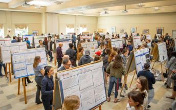 wide view of projects being presented on sandwich boards with many people in a big room