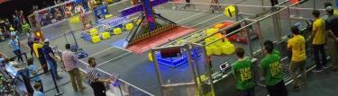A basketball court setup for a robotics competition. Teams watching the competition and people in the stands.