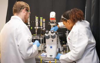 A photo of two students in lab coats adjusting a microscope